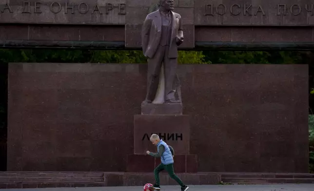 A boy plays next to a statue of Lenin, with the words "Board of Honor" written in Cyrillic in Romanian and Russian in Chisinau, Moldova, Friday, Nov. 1, 2024. (AP Photo/Vadim Ghirda)