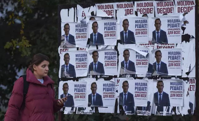 A woman walks past posters displaying Alexandr Stoianoglo, presidential candidate of the Socialists' Party of Moldova (PSRM) in Chisinau, Moldova, Friday Nov. 1, 2024. (AP Photo/Vadim Ghirda)