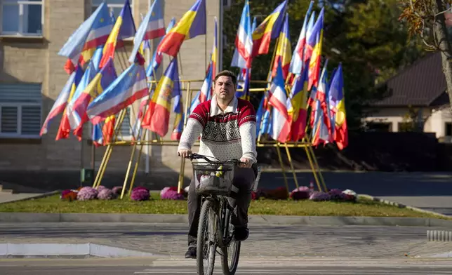 A man cycles backdropped by Moldovan and Gagauz flags in Comrat, the capital of Gagauzia, an autonomous part of Moldova, Saturday, Nov. 2, 2024, ahead of a presidential election runoff taking place on Sunday. (AP Photo/Vadim Ghirda)