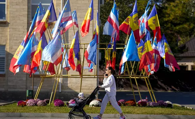 A woman pushes a baby stroller backdropped by moldovan and gagauz flags in Comrat, the capital of Gagauzia, an autonomous part of Moldova, Saturday, Nov. 2, 2024, ahead of a presidential election runoff taking place on Nov. 3. (AP Photo/Vadim Ghirda)