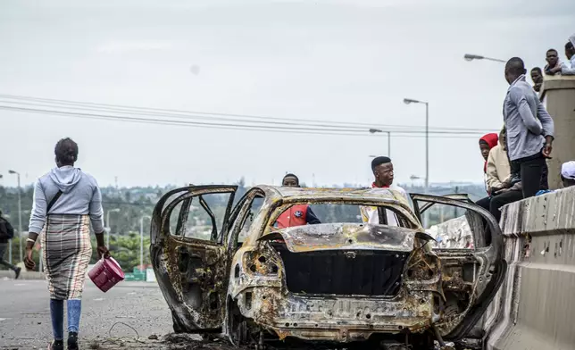 Pedestrians alongside burnt out vehicle Wednesday, Nov. 6, 2024 in Mozambique's capital Maputo, in protests that have engulfed the country after the opposition rejected the results of the country's polls which saw the Frelimo party extend its 58-year rule. (AP Photo/Carlos Uqueio)