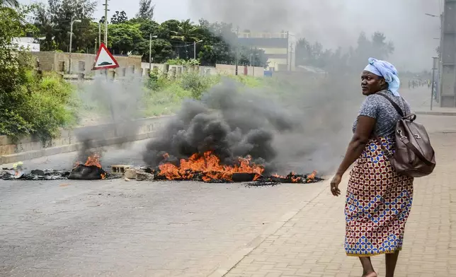 A woman walks past a barricade set fire by protesters in Maputo, Mozambique, Thursday, Nov. 7, 2024. Protesters dispute the outcome of the Oct. 9 elections that saw the ruling Frelimo party extend its 49-year rule. (AP Photo/Carlos Uqueio)