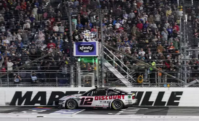 Ryan Blaney (12) takes the checkered flag to win a NASCAR Cup Series auto race at Martinsville Speedway in Martinsville, Va., Sunday, Nov. 3, 2024. (AP Photo/Chuck Burton)