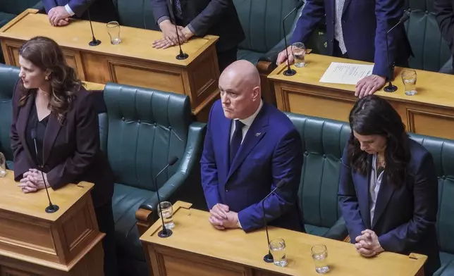 New Zealand Prime Minister Christopher Luxon, center, stands in silence ahead of making a "formal and unreserved" apology in Parliament for the widespread abuse, torture and neglect of hundreds of thousands of children and vulnerable adults in care, in Wellington, New Zealand Tuesday, Nov. 12, 2024. (AP Photo/Charlotte Graham-McLay )