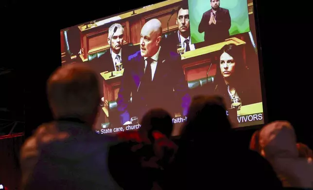 New Zealand's Prime Minister Christopher Luxon is shown on a screen as he makes a "formal and unreserved" apology in Parliament for the widespread abuse, torture and neglect of hundreds of thousands of children and vulnerable adults in care, in Wellington, New Zealand, Tuesday, Nov. 12, 2024. (Lawrence Smith/Stuff via AP )