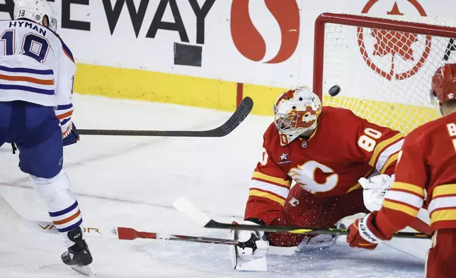 Edmonton Oilers' Zach Hyman, left, scores against Calgary Flames goalie Dan Vladar (80) during third -period NHL hockey game action in Calgary, Alberta, Sunday, Nov. 3, 2024. (Jeff McIntosh/The Canadian Press via AP)