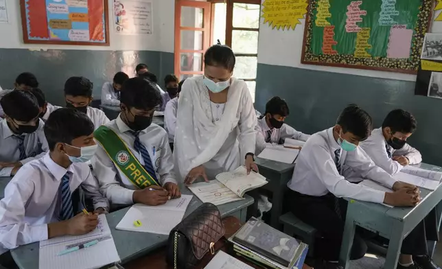 A teacher and students wear mask to protect themselves from poor air quality due to increasing smog in the city as they attend their school, in Lahore, Pakistan, Monday, Nov. 4, 2024. (AP Photo/K.M. Chaudary)