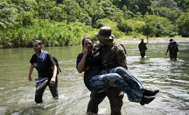 A Panamanian border police officer carries Adriana Rodriguez to banks of the Tuquesa River, near Bajo Chiquito, Panama, after she walked with other Venezuelan migrants across the Darien Gap from Colombia on their way north to the United States, Saturday, Nov. 9, 2024. (AP Photo/Matias Delacroix)