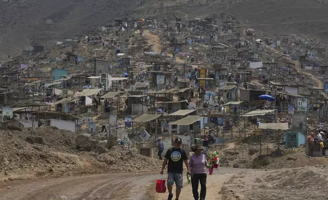 A couple arrive to the Nueva Esperanza cemetery to decorate family graves marking the Day of the Dead, in the Villa Maria community of Lima, Peru, Friday, Nov. 1, 2024. (AP Photo/Guadalupe Pardo)