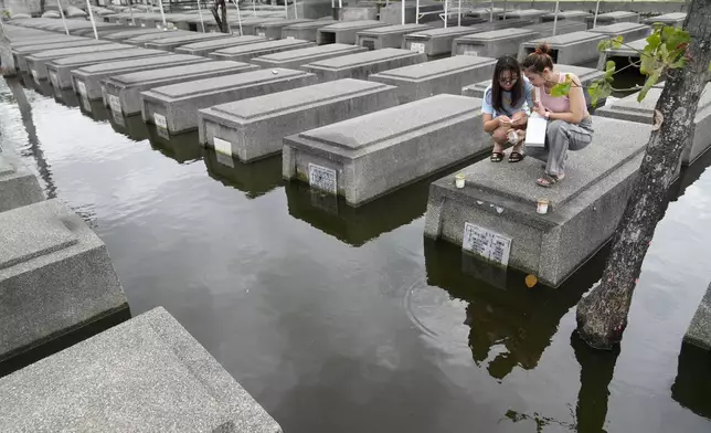 Women place candles on the half-submerged tomb of family members at flood-prone Holy Spirit Memorial Park in Masantol, Pampanga province, Philippines after heavy rains from recent tropical storm Trami caused water levels to become higher than usual ahead of All Saints Day, Thursday Oct. 31, 2024. (AP Photo/Aaron Favila)