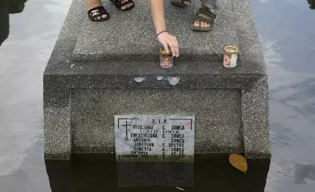 A woman covers candles placed on the half-submerged tomb of family members at flood-prone Holy Spirit Memorial Park in Masantol, Pampanga province, Philippines after heavy rains from recent tropical storm Trami caused water to become higher than usual, ahead of All Saints Day, Thursday Oct. 31, 2024. (AP Photo/Aaron Favila)