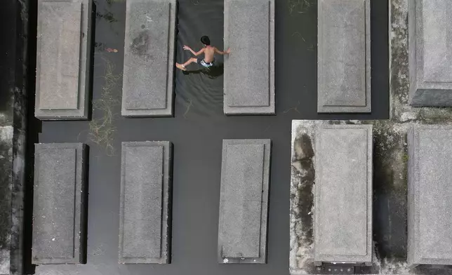 A boy plays on top of tombs submerged at flood-prone Holy Spirit Memorial Park in Masantol, Pampanga province, Philippines after heavy rains from recent tropical storm Trami caused water to become higher than usual, ahead of All Saints Day, Thursday Oct. 31, 2024. (AP Photo/Aaron Favila)