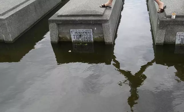 A woman walks on top of half-submerged tombs at flood-prone Holy Spirit Memorial Park, in Masantol, Pampanga province, Philippines after heavy rains from recent tropical storm Trami caused water to become higher than usual ahead of All Saints Day, Thursday Oct. 31, 2024. (AP Photo/Aaron Favila)