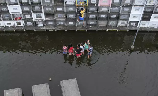 People visit the tomb of family members at flood-prone Holy Spirit Memorial Park in Masantol, Pampanga province, Philippines after heavy rains from recent tropical storm Trami caused water levels to become higher than usual ahead of All Saints Day, Thursday Oct. 31, 2024. (AP Photo/Aaron Favila)