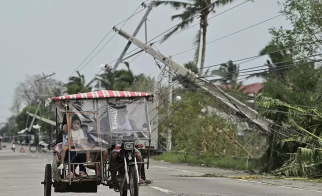 Residents riding a tricycle pass by toppled electrical posts caused by Typhoon Yinxing, locally called Marce, in Camalaniugan, Cagayan province, northern Philippines on Friday Nov. 8, 2024. (AP Photo/Noel Celis)