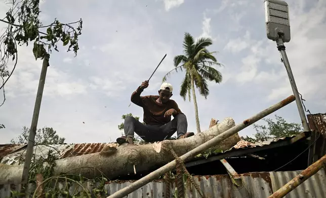 A man tries to clear a tree trunk after it fell on the roof of his house after Typhoon Yinxing, locally called Marce, blows past in Gattaran, Cagayan province, northern Philippines on Friday Nov. 8, 2024. (AP Photo/Noel Celis)