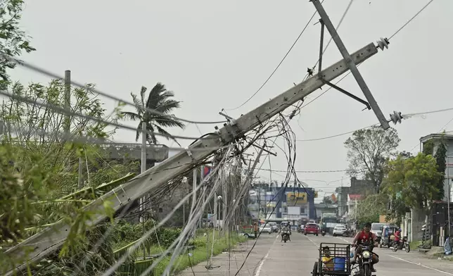 Residents riding a tricycle pass by toppled electrical post caused by Typhoon Yinxing, locally called Marce, in Camalaniugan, Cagayan province, northern Philippines on Friday, Nov. 8, 2024. (AP Photo/Noel Celis)