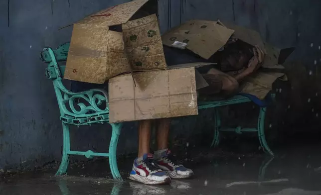 People at a bus stop shield themselves with cardboard amid wind and rain during the passage of Hurricane Rafael in Havana, Cuba, Wednesday, Nov. 6, 2024. (AP Photo/Ramon Espinosa)