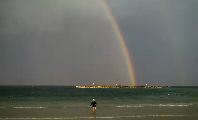 A rainbow stretches across the sky as a woman walks along the shore after swimming at the Mediterranean sea, in Tel Aviv, Israel, Monday, Nov. 4, 2024. (AP Photo/Francisco Seco)