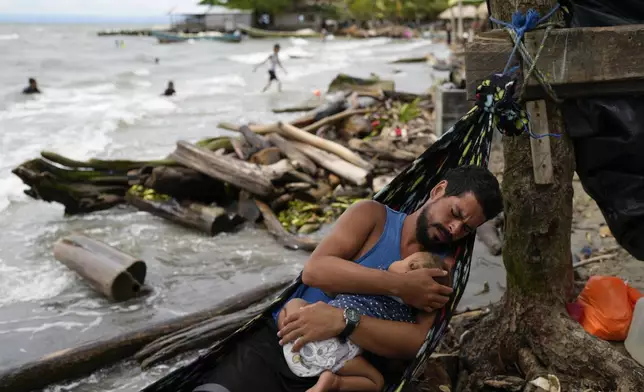 Jackson Vargas, who left Venezuela after the country's disputed election, holds his daughter along the shore in Necocli, Colombia, as they save money ahead of traversing the Darien Gap, Monday, Oct. 14, 2024. (AP Photo/Matias Delacroix)