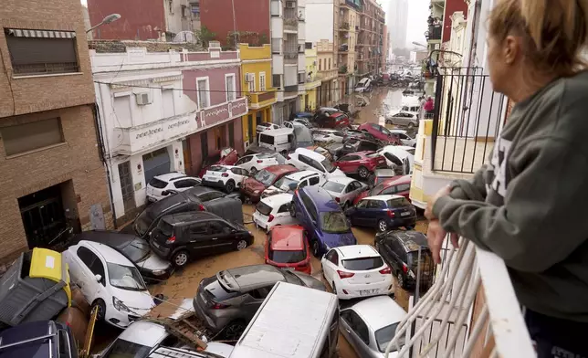 A woman looks out from her balcony as vehicles are trapped in the street during flooding in Valencia, Wednesday, Oct. 30, 2024. (AP Photo/Alberto Saiz)