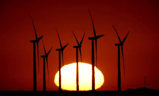 Wind turbines at the Buckeye Wind Energy are diffused by heat vapors as they are silhouetted against the rising sun, Monday, Sept. 30, 2024, near Hays, Kan. (AP Photo/Charlie Riedel)