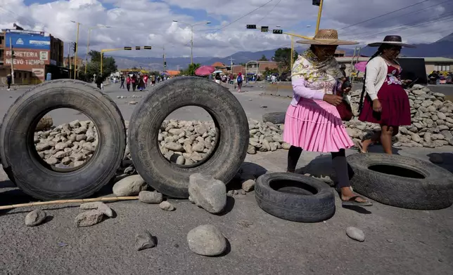 Women walk past a barricade of debris set up by supporters of former President Evo Morales who are blocking roads to prevent him from facing a criminal investigation over allegations of abuse of a minor and to protest an alleged assassination attempt near Cochabamba, Bolivia, Monday, Oct. 28, 2024. (AP Photo/Juan Karita)