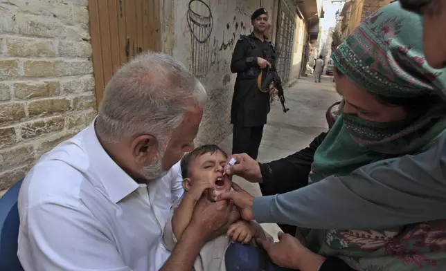 A police officer stands guard as a health worker, right, administers a polio vaccine to a child in a neighbourhood of Peshawar, Pakistan, Monday, Oct. 28, 2024. (AP Photo/Mohammad Sajjad)