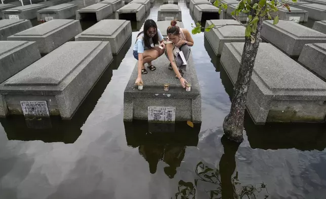 Women place candles on the half-submerged tomb of family members at flood-prone Holy Spirit Memorial Park in Masantol, Pampanga province, Philippines after heavy rains from recent tropical storm Trami caused water to become higher than usual, ahead of All Saints Day, Thursday Oct. 31, 2024. (AP Photo/Aaron Favila)