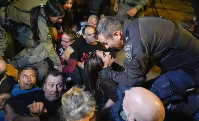 A police officer shouts at a woman as people protesting against Prime Minister Benjamin Netanyahu's government and calling for the release of hostages held in the Gaza Strip by the Hamas militant group, are dispersed near the Prime Minister's residence in Jerusalem, Monday, Oct. 28, 2024. (AP Photo/Ohad Zwigenberg)