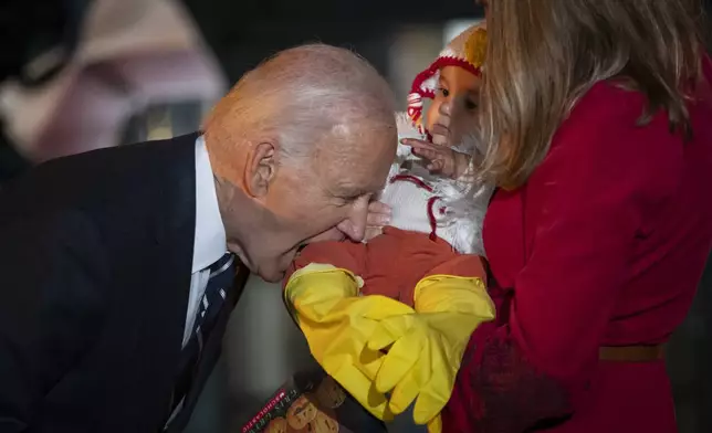 President Joe Biden jokingly bites the leg of a baby, as he and first lady Jill Biden host local area students, military-connected children, and neighborhood families for trick-or-treating, ahead of Halloween on Thursday, at the South Lawn of the White House in Washington Wednesday, Oct. 30, 2024. (AP Photo/Ben Curtis)