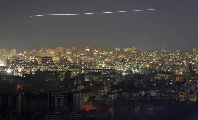 In this photo taken with slow shutter speed, a Middle East Airlines airplane flies over the capital Beirut, as fire rises from an Israeli airstrike in Dahiyeh, Lebanon, Friday, Oct. 25, 2024. (AP Photo/Hassan Ammar)