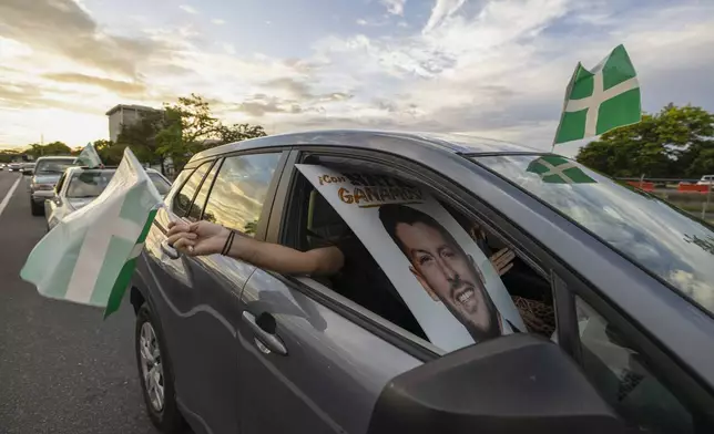 A supporter waves a Puerto Rican Independence Party flag while holding a campaign poster promoting the Citizens' Victory Movement mayoral candidate Manuel Natal, during a caravan in San Juan, Puerto Rico, Friday, Nov. 1, 2024. (AP Photo/Alejandro Granadillo)