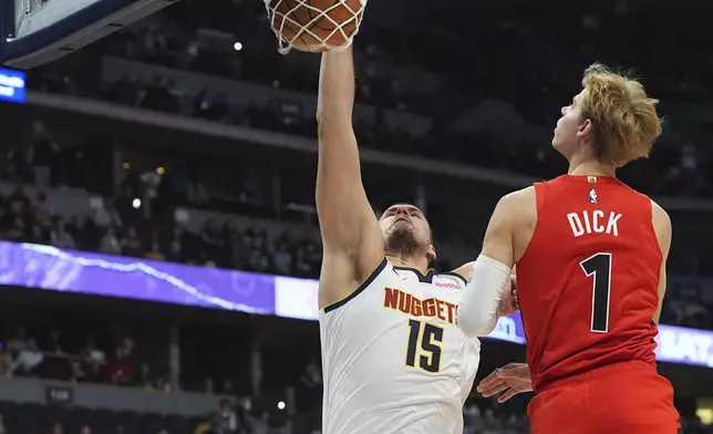 Denver Nuggets center Nikola Jokic, left, dunks as Toronto Raptors guard Gradey Dick (1) defends in the first half of an NBA basketball game Monday, Nov. 4, 2024, in Denver. (AP Photo/David Zalubowski)