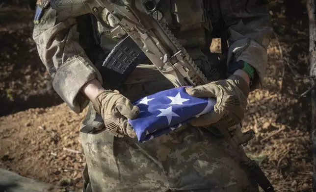 A 25-year-old volunteer fighter with callsign Dima from Texas, who serves with the 23rd separate rifle battalion of Ukraine's Armed Forces, holds the U.S. flag that he always carry with him at the front line in the Kharkiv region, Ukraine, Saturday, Oct. 26, 2024. (AP Photo/Efrem Lukatsky)