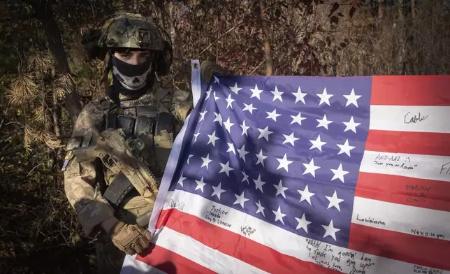 A 25-year-old volunteer fighter with callsign Dima from Texas, who serves with the 23rd separate rifle battalion of Ukraine's Armed Forces, holds the U.S. flag in his position near the front line in the Kharkiv region, Ukraine, Saturday, Oct. 26, 2024. (AP Photo/Efrem Lukatsky)