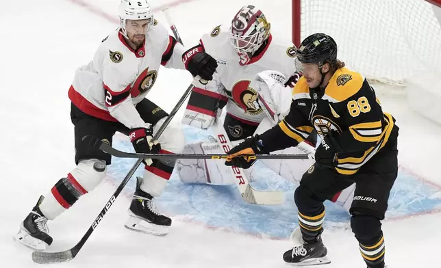 Boston Bruins' David Pastrnak (88) tries to control the puck against Ottawa Senators' Artem Zub (2) and Linus Ullmark (35) during the first period of an NHL hockey game, Saturday, Nov. 9, 2024, in Boston. (AP Photo/Michael Dwyer)