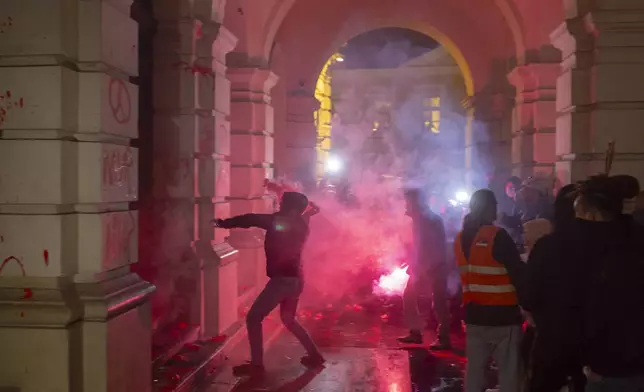 A protester attempts to throw a flare into the City Hall building during a protest in rage over last week's collapse of a concrete canopy at the railway station that killed 14 people, in Novi Sad, Serbia, Tuesday, Nov. 5, 2024. (AP Photo/Marko Drobnjakovic)