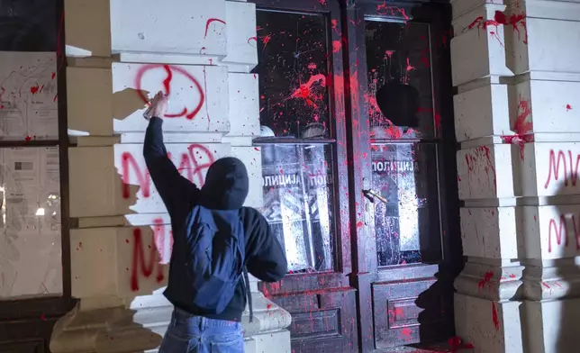 A protester paints grafitti on the City Hall building during a protest in rage over last week's collapse of a concrete canopy at the railway station that killed 14 people, in Novi Sad, Serbia, Tuesday, Nov. 5, 2024. (AP Photo/Marko Drobnjakovic)