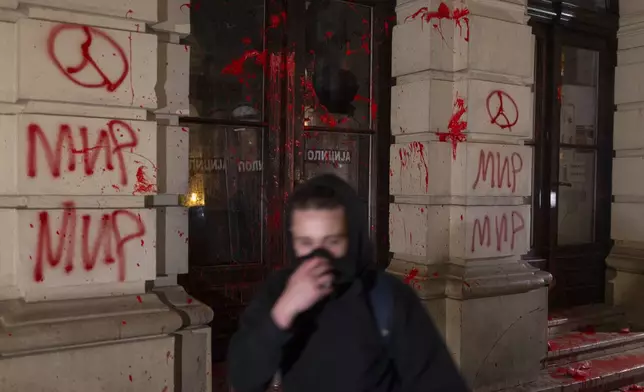 A protester passes by the City Hall building covered in red paint during a protest in Novi Sad, Serbia, Tuesday, Nov. 5, 2024. (AP Photo/Marko Drobnjakovic)