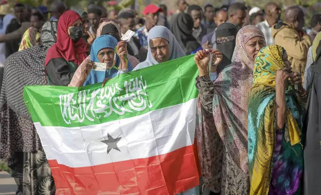 A woman displays the Somaliland flag as people queue to cast their votes during the 2024 Somaliland presidential election at a polling station in Hargeisa, Somaliland, Wednesday, Nov. 13,2024. (AP Photo/Abdirahman Aleeli)