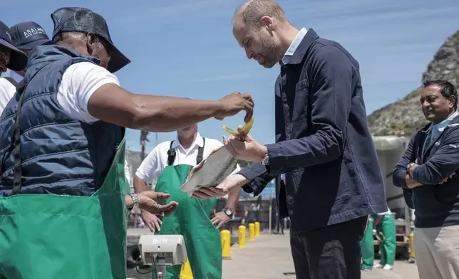 Britain's Prince William, center, is handed a fish as he speaks to local fisherman in Kalk Bay Harbour, near Cape Town, South Africa Thursday, Nov. 7, 2024. (Gianluigi Guercia/Pool Photo via AP)