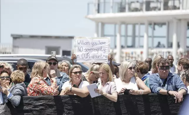 A person holds a placard that reads "William, you have no sovereignty in our country" while a crowd gathers to see Britain's Prince William (unseen) meeting local fisherman in Kalk Bay Harbour, near Cape Town, South Africa Thursday, Nov. 7, 2024. (Gianluigi Guercia/Pool Photo via AP)