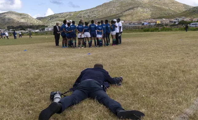 A photographer lies on the ground to take a picture of Britain's Prince William greeting pupils at the Ocean View Secondary School in Cape Town, South Africa, Monday, Nov. 4, 2024. (AP Photo/Jerome Delay-pool)