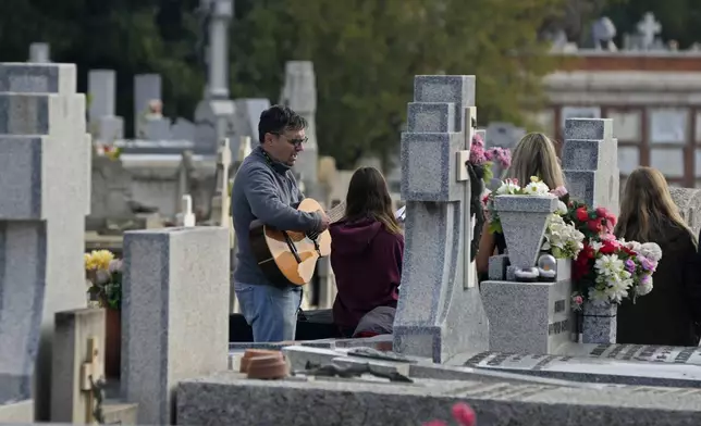 A man sings and plays a guitar as others gather around a grave in the Almudena cemetery during All Saints Day, a Christian holiday to reflect on the saints and deceased relatives, Madrid, Spain, Friday, Nov. 1, 2024. (AP Photo/Paul White)