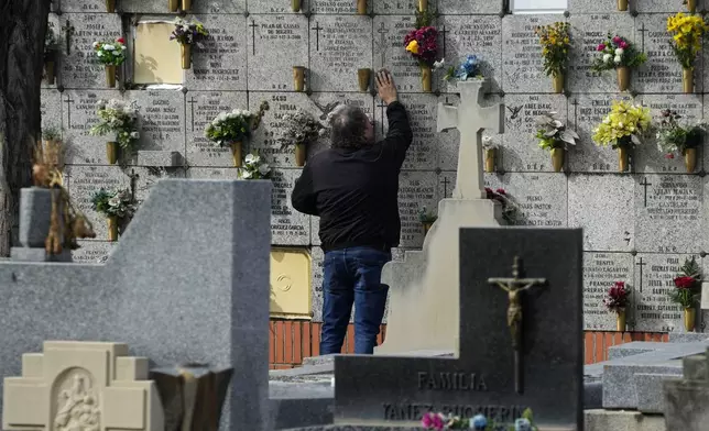 A man touches the plaque of a niche in the Almudena cemetery during All Saints Day, a Christian holiday to reflect on the saints and deceased relatives, Madrid, Spain, Friday, Nov. 1, 2024. (AP Photo/Paul White)