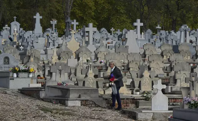 A woman walks between gravestones carrying flowers in the Almudena cemetery during All Saints Day, a Christian holiday to reflect on the saints and deceased relatives, Madrid, Spain, Friday, Nov. 1, 2024. (AP Photo/Paul White)