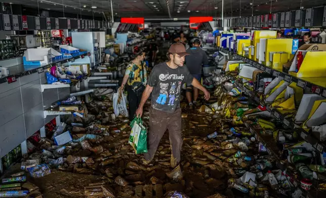 People pick up goods in a supermarket affected by the floods in Valencia, Spain, Thursday, Oct. 31, 2024. (AP Photo/Manu Fernandez)