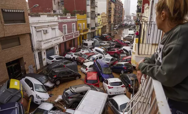 A woman looks out from her balcony as vehicles are trapped in the street during flooding in Valencia, Wednesday, Oct. 30, 2024. (AP Photo/Alberto Saiz)