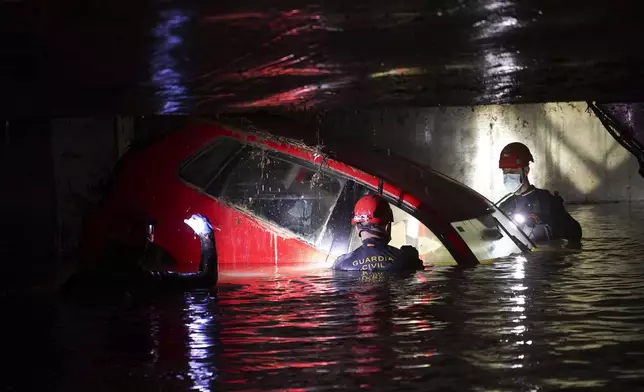 Civil Guards walk in a flooded indoor car park to check cars for bodies after floods in Paiporta, near Valencia, Spain, Monday, Nov. 4, 2024. (AP Photo/Alberto Saiz)